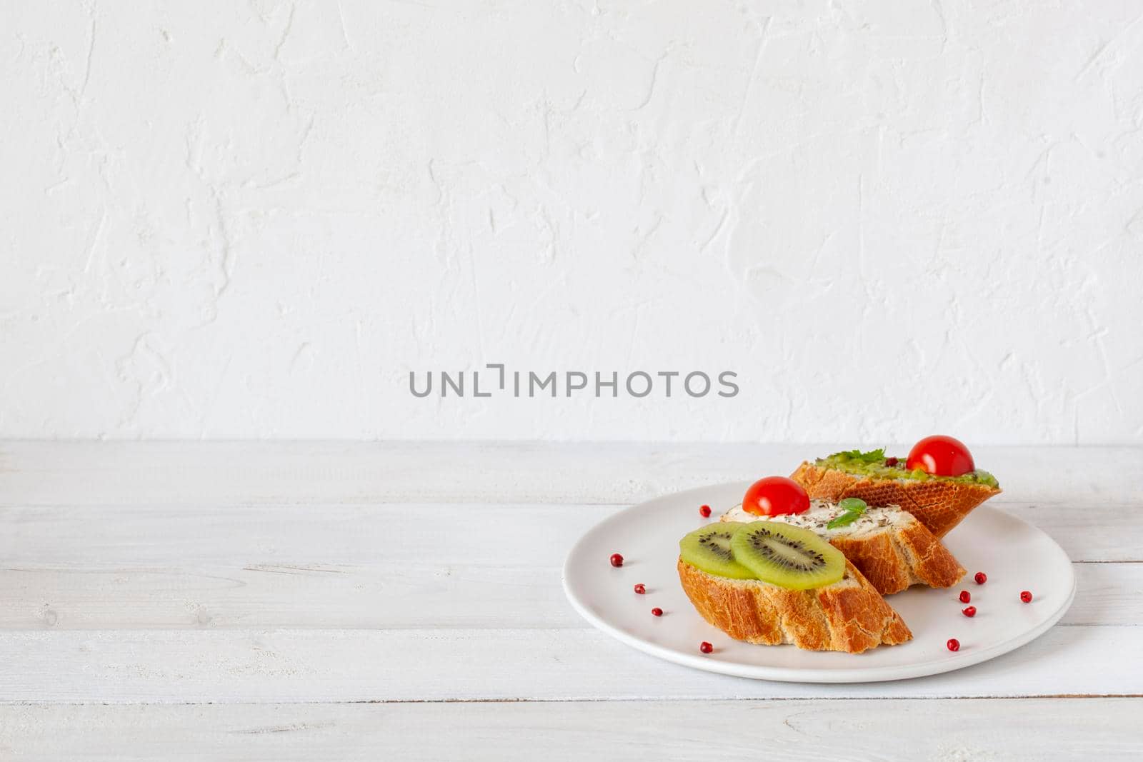 three homemade bright mini sandwichs with cream cheese and vegetables, on a white plate on wooden background, side view, copy space