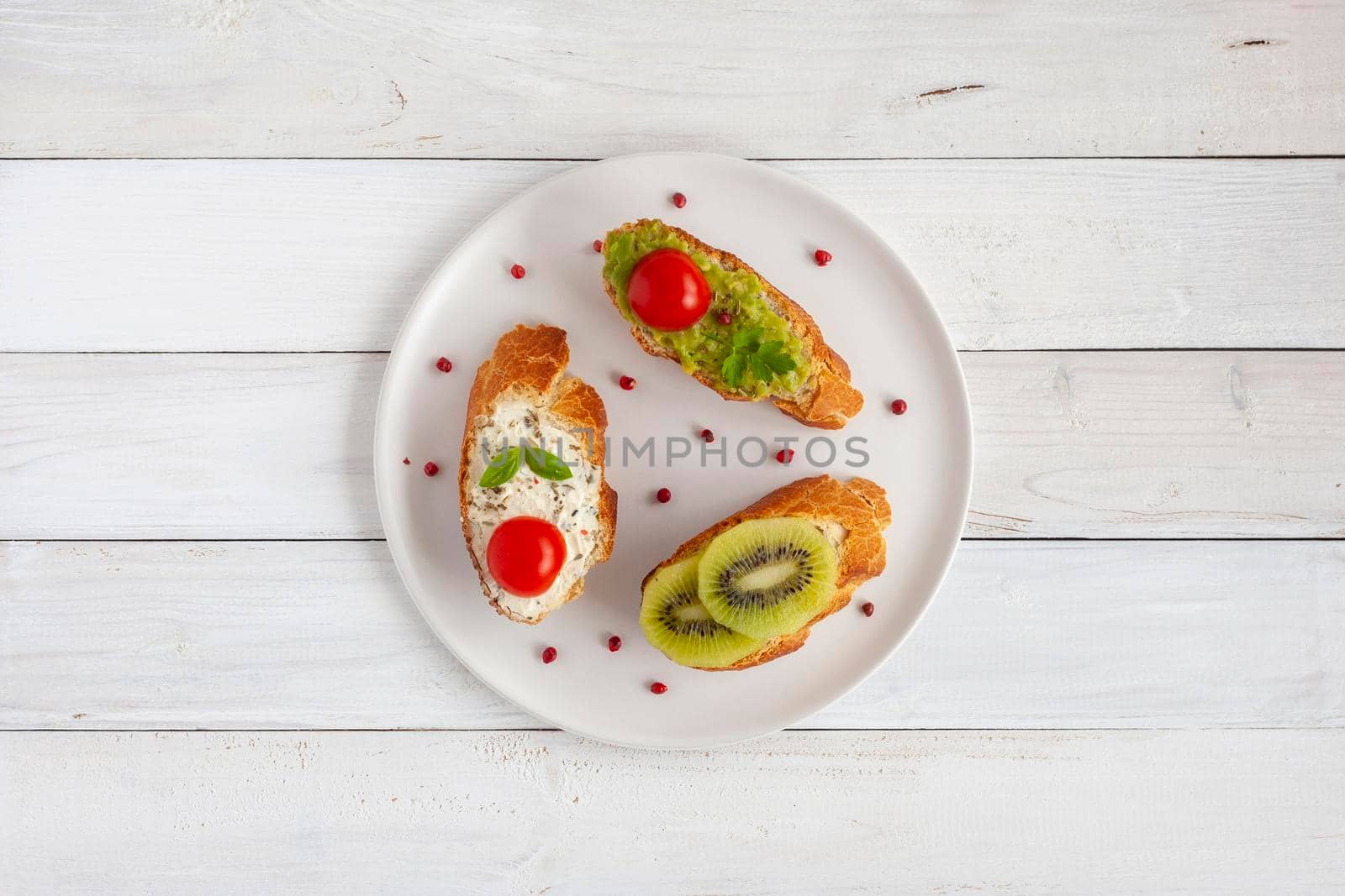 three homemade bright mini sandwichs with cream cheese and vegetables, on a white plate on wooden background, top view