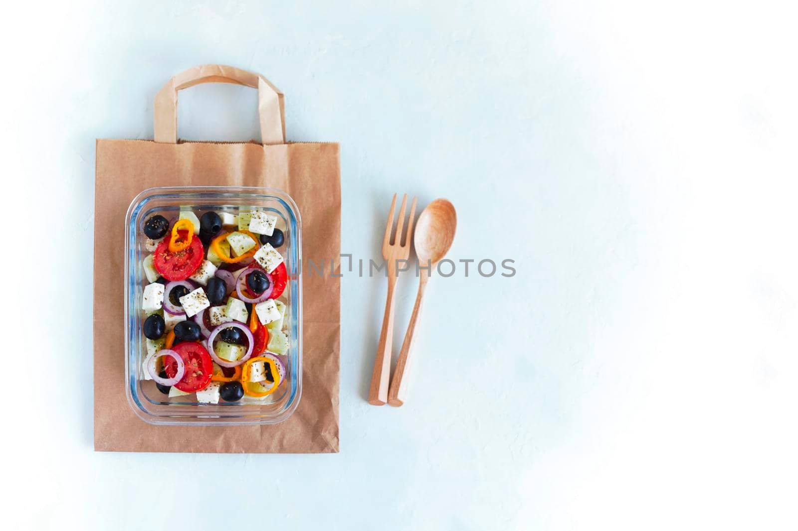 container with greek salad, wooden cutlery, on white background, top view, copy space, concept of healthy food and zero waste, copy space