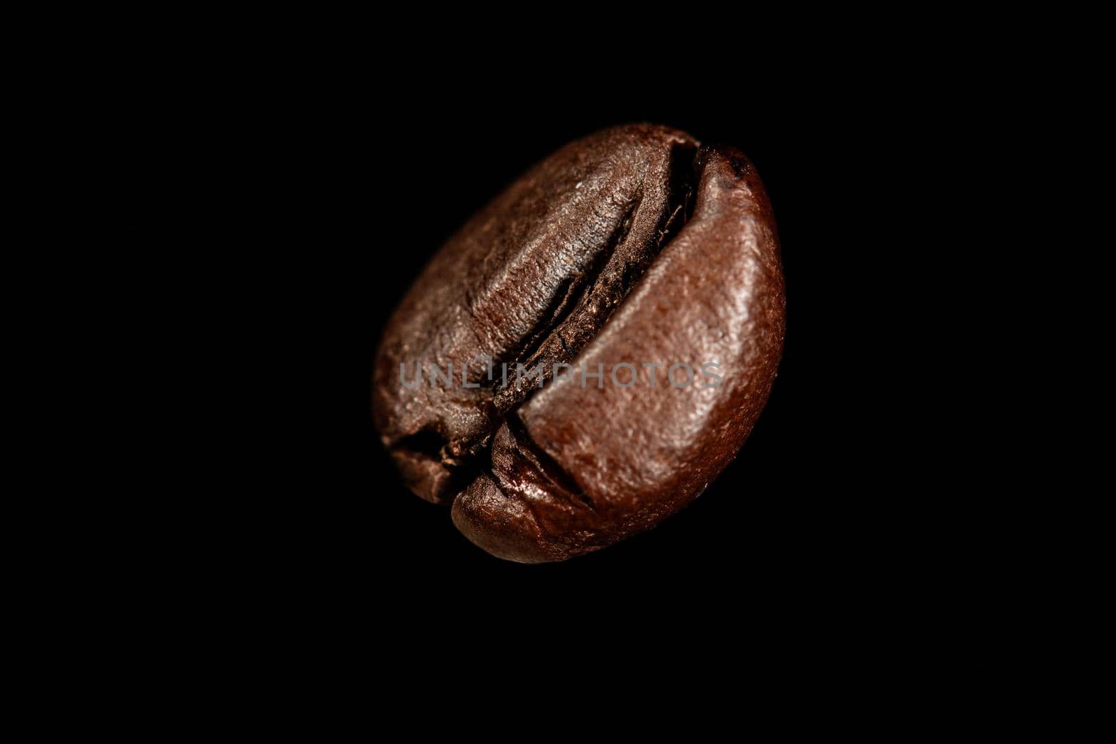 One single dark roasted coffee bean on a black colored surface.