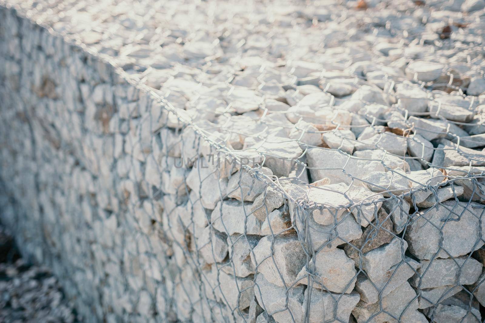 strengthening the slope with stones behind the wire. grey texture. construction. Granite stones behind a metal grate