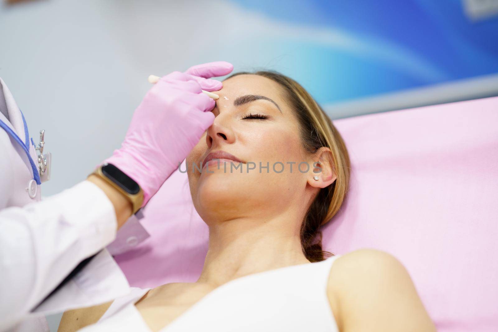 Aesthetic doctor painting on the face of his middle-aged patient the areas to be treated with botulinum toxin.