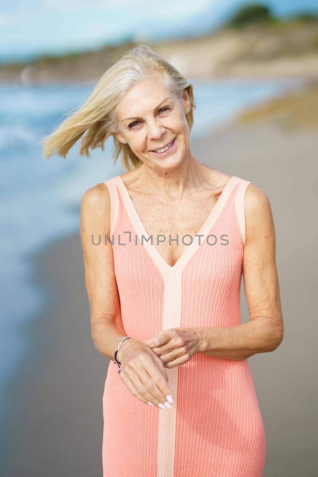 Beautiful senior woman walking along the shore of a tropical beach, wearing a nice orange dress. Elderly female enjoying her retirement at a seaside retreat.