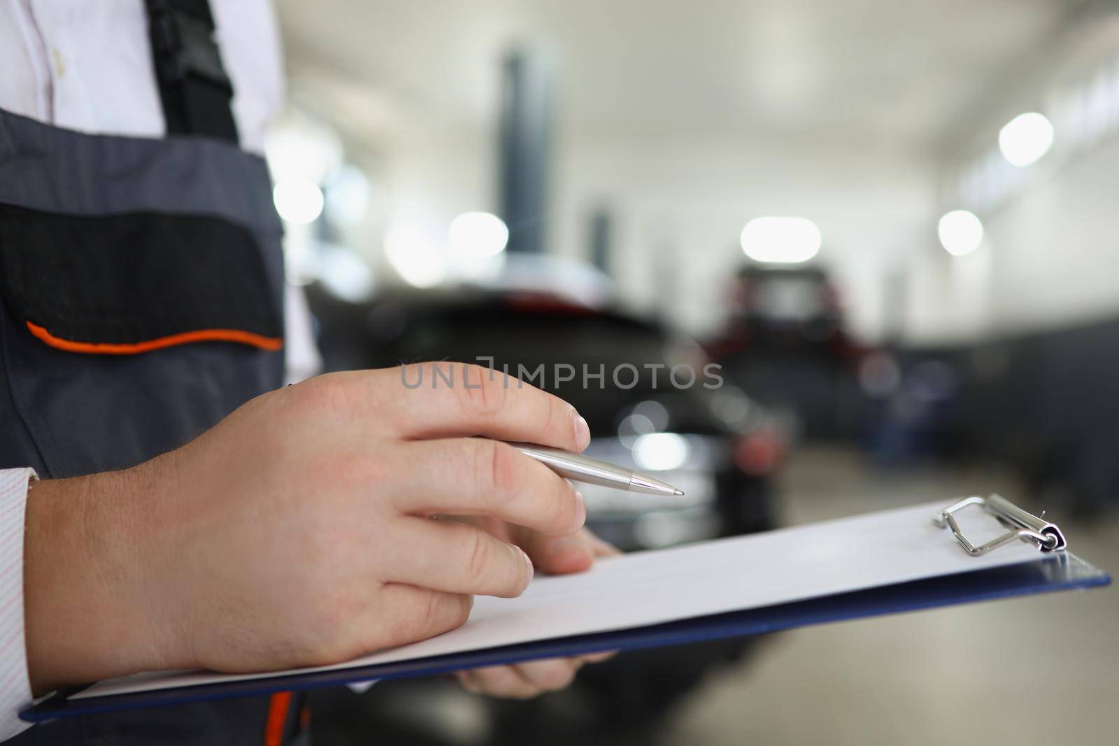 Close-up of male service worker fill maintenance documentation after fixing car. Professional mechanic work in garage. Car service, pit stop, handy concept