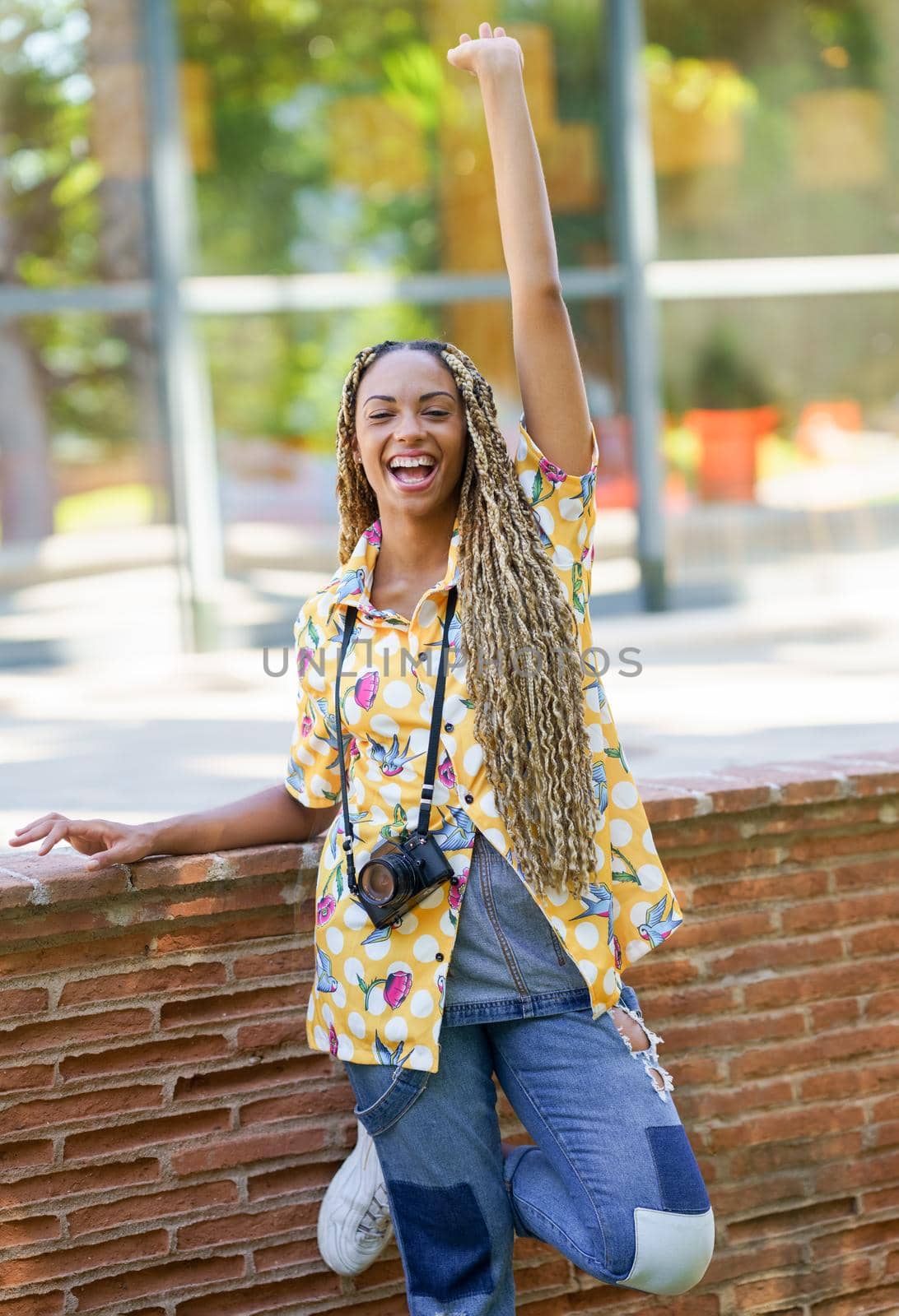 Black female with African braids, raising her arm in joy. Girl holding a camera. by javiindy