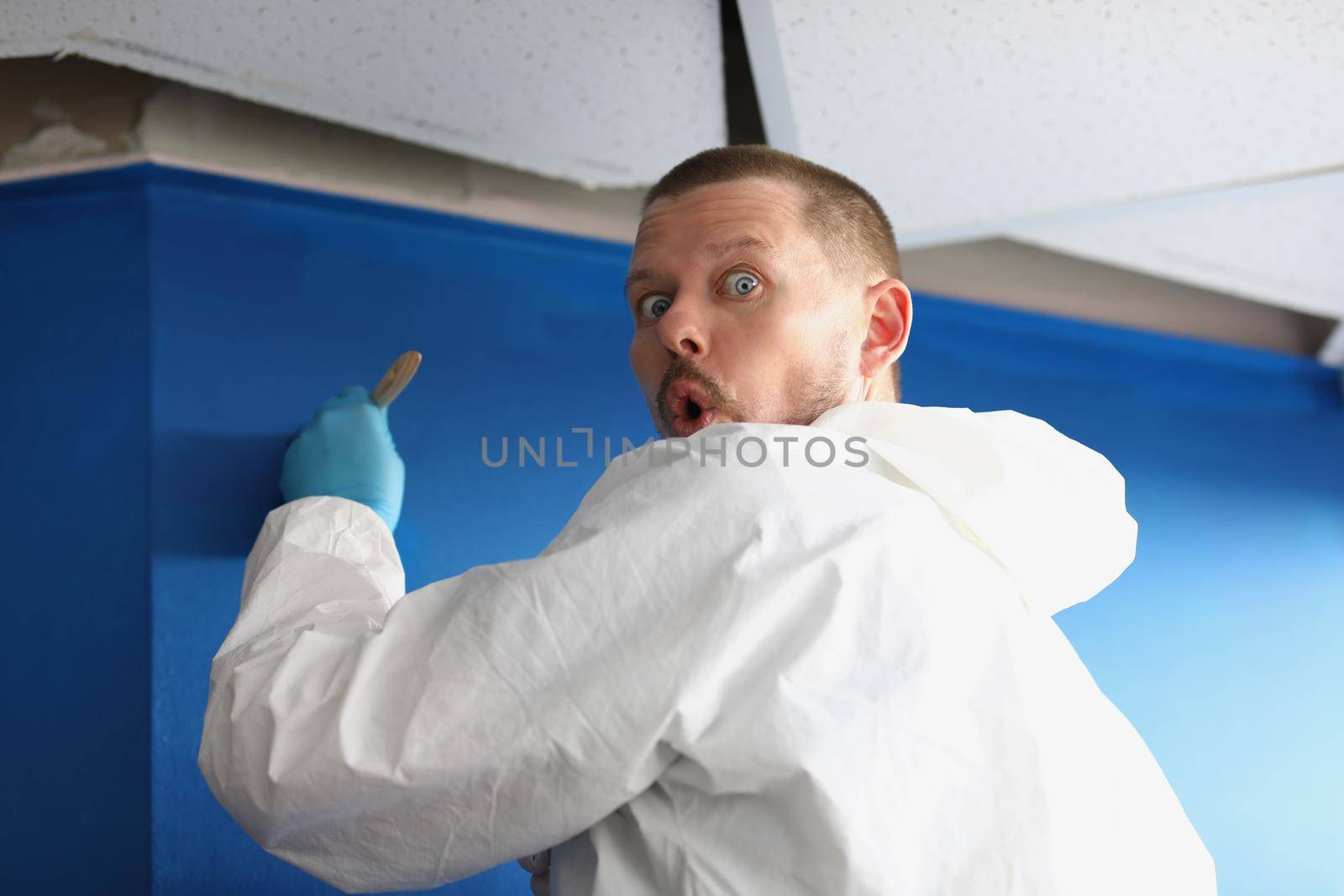 Male worker caught by surprise painting wall in blue colour by kuprevich