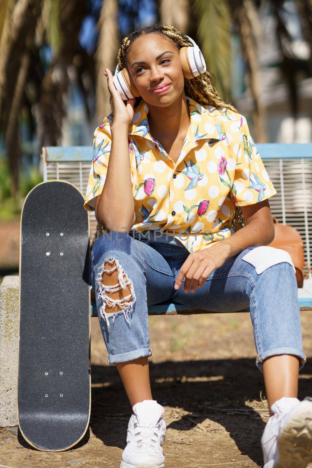 Young smiling African woman with skateboard Mixed-race girl relaxing after riding skateboard listening to the music outdoors.