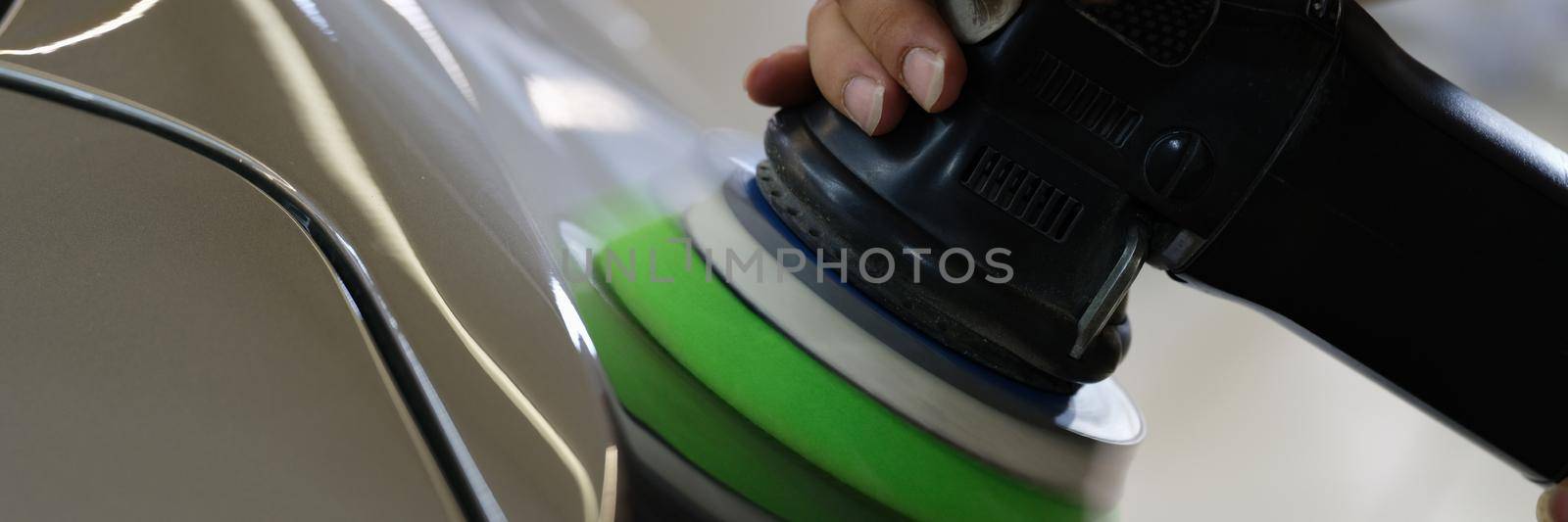 Mechanic polishing headlights of car using special machine closeup by kuprevich