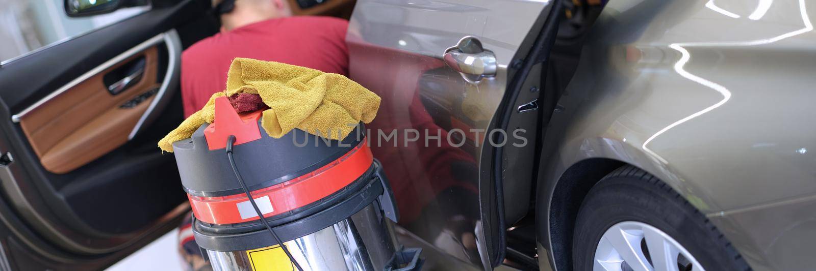 Vacuum cleaner standing near car washer man closeup. Car cleaning service concept