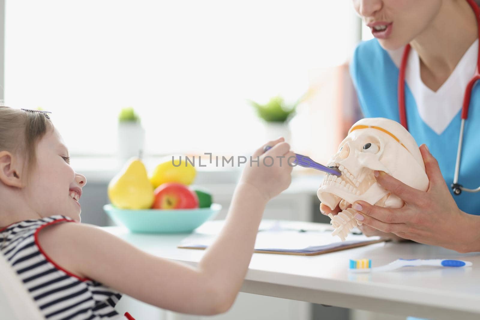 Female doctor let little girl patient play with fake plastic skull by kuprevich