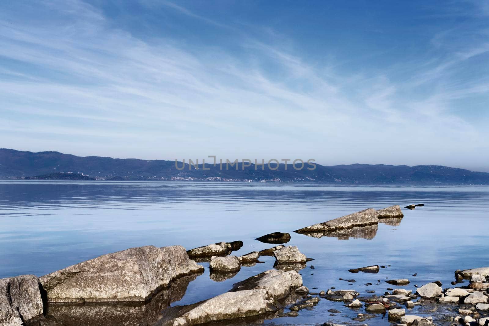 Rocks in the clear  water of Trasimeno lake in Italy , in the background old small town