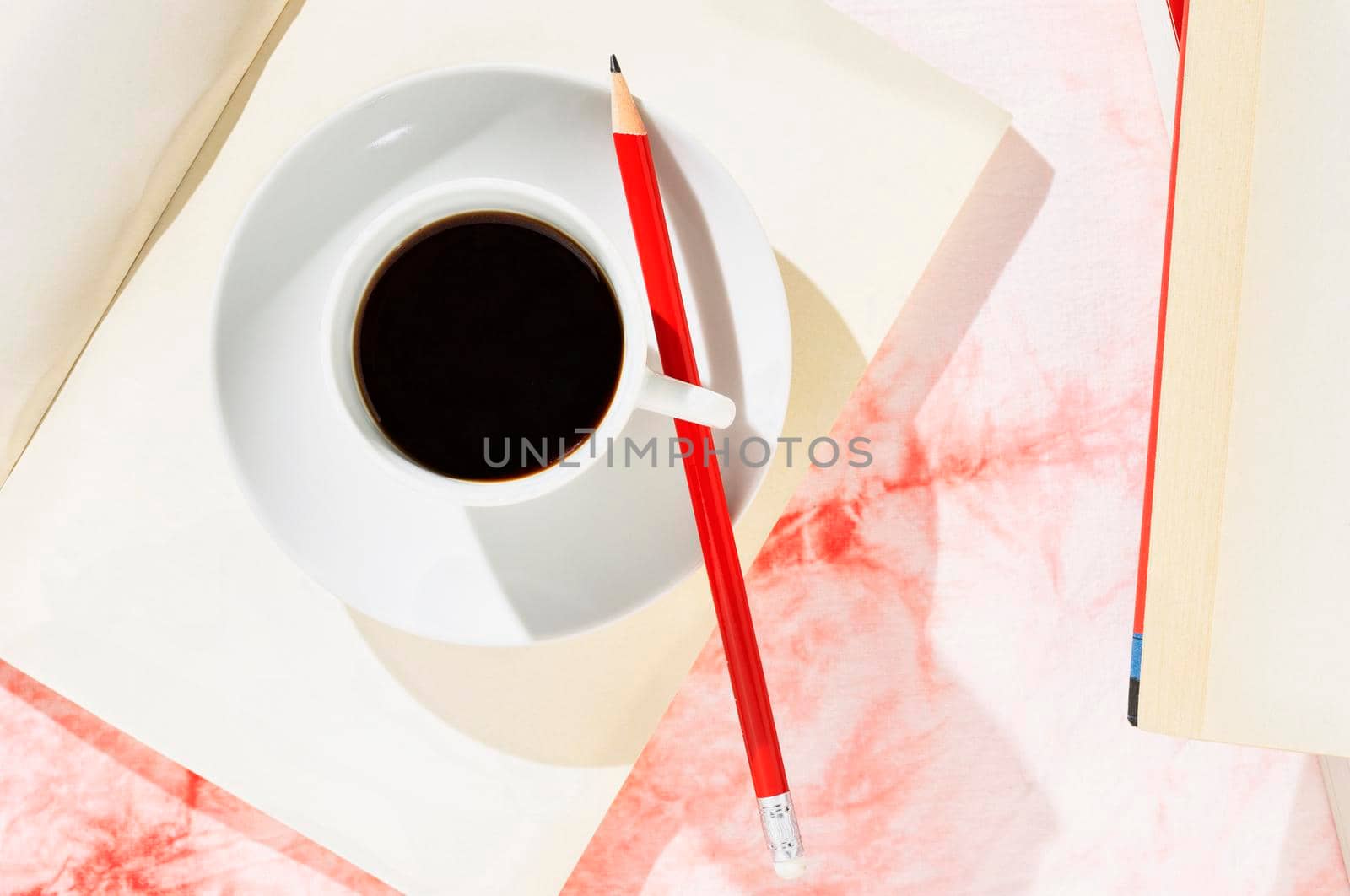 White cup of coffee  with red pencil on opened book , white and red background