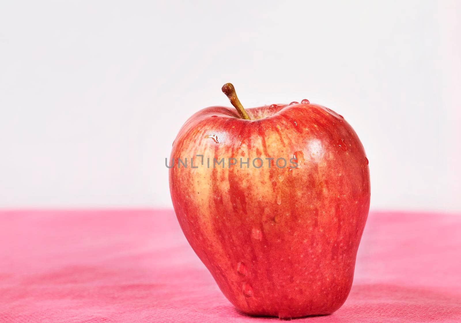 Red apple with waters drops on colored background 
