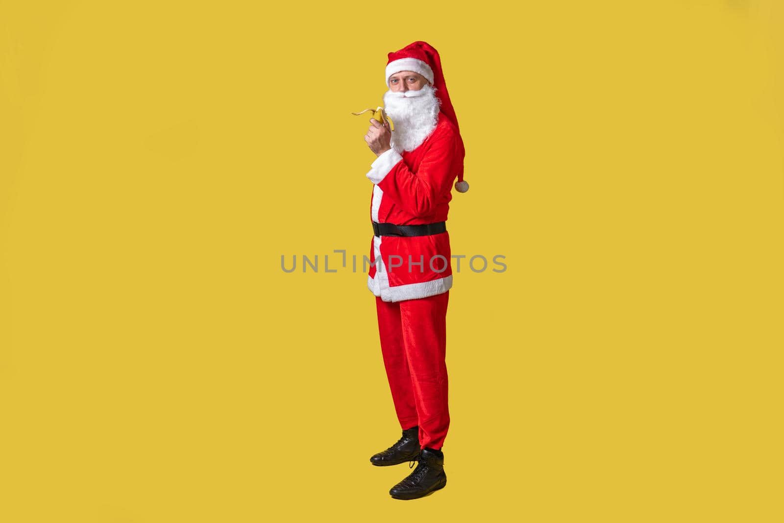 Santa claus yellow funny big, person fun happy. Fashionable bearded Caucasian, time eats a banana with his right hand