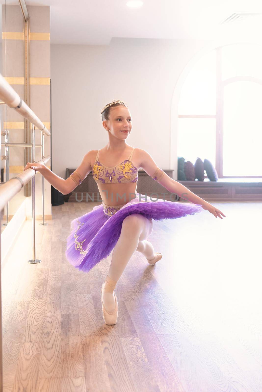 Close-up of a smiling teenage girl wearing pointe shoes in ballet class, near a frame and large mirror doing exercises and stretching by Nickstock
