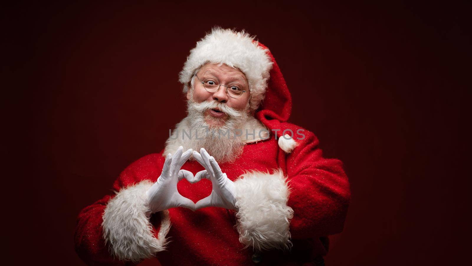 Festive noel seasonal kind positive stylish aged Santa look at camera make nice smile and shape heart with fingers hands on dark background