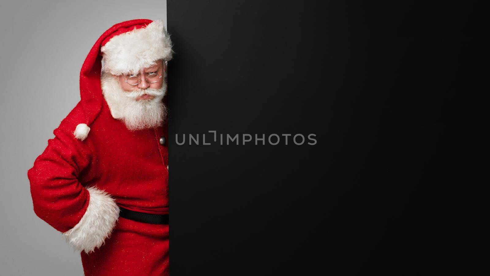 Santa Claus with black paper billboard with copy space for text , surprised facial expression