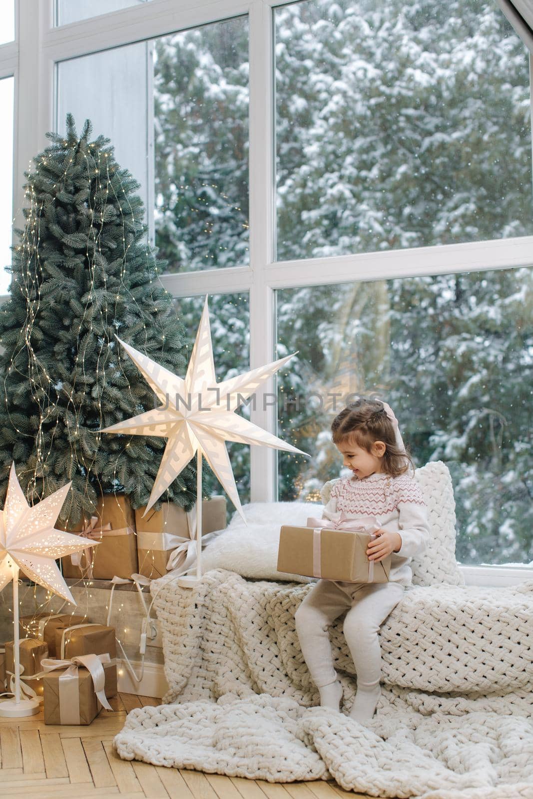 Happy beautiful girl take present in front of big window. Christmas time. It's snow outside. Christmas tree by Gritsiv