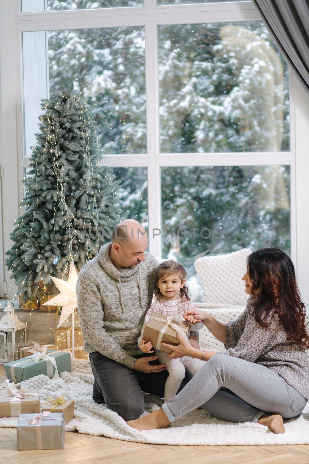 Gradparents hug her granddaughter near fir tree at home. Christmas mood of happy people.