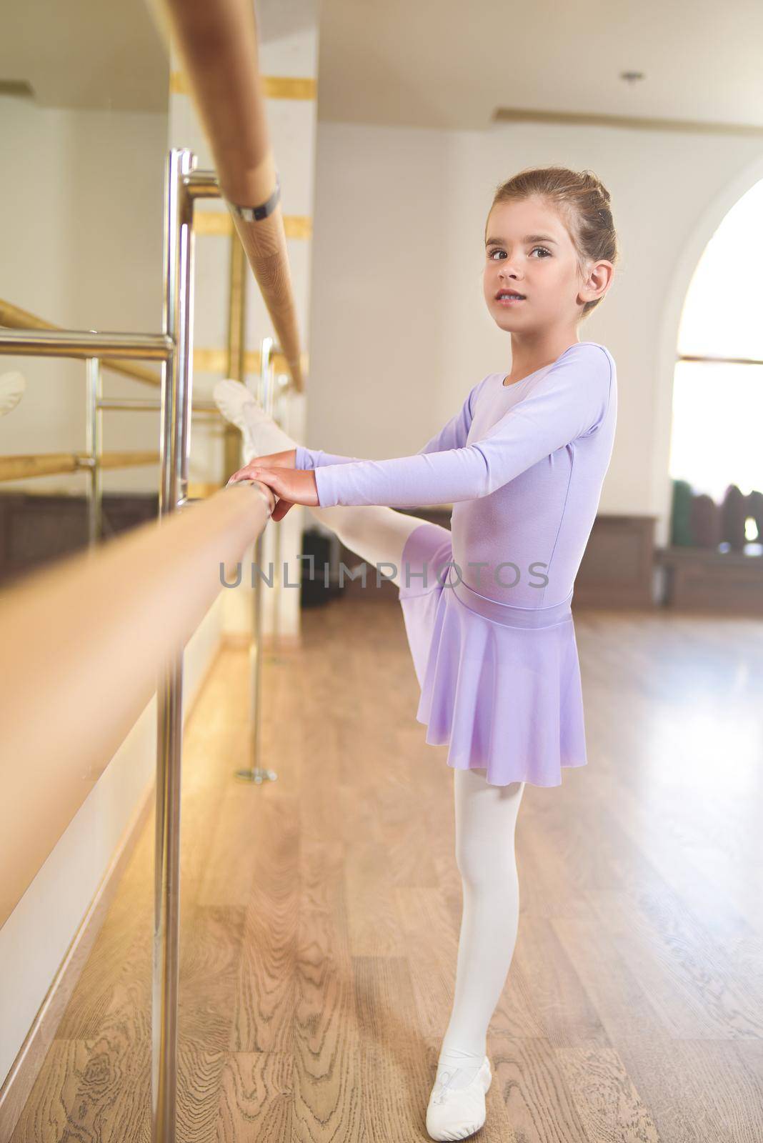little girl wear pointe shoes in ballet class near frame and large mirror doing exercises and stretching by Nickstock