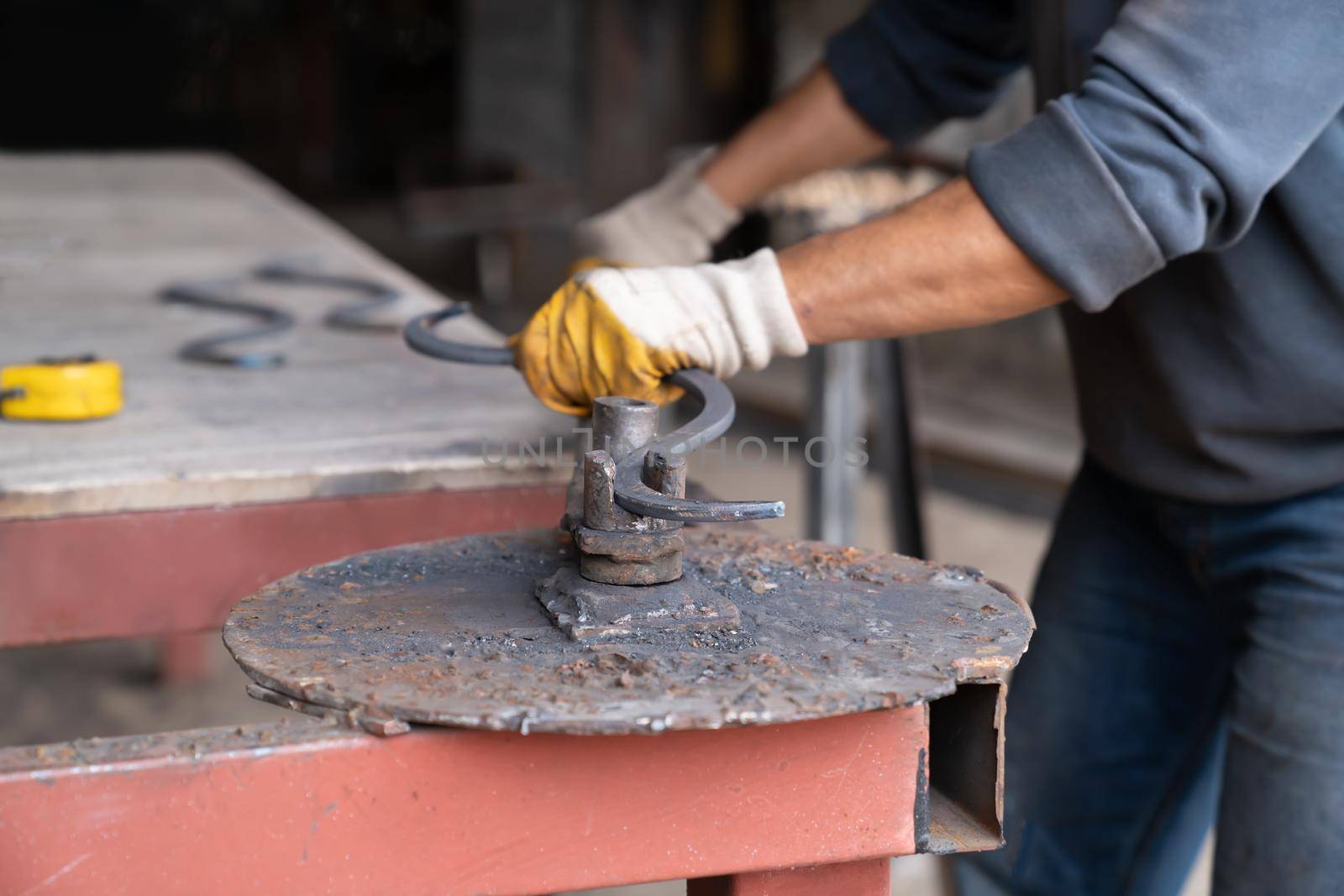 Man bends metal part creating curved shape using special machine. Blacksmith shop - metal workshop. Close-up.