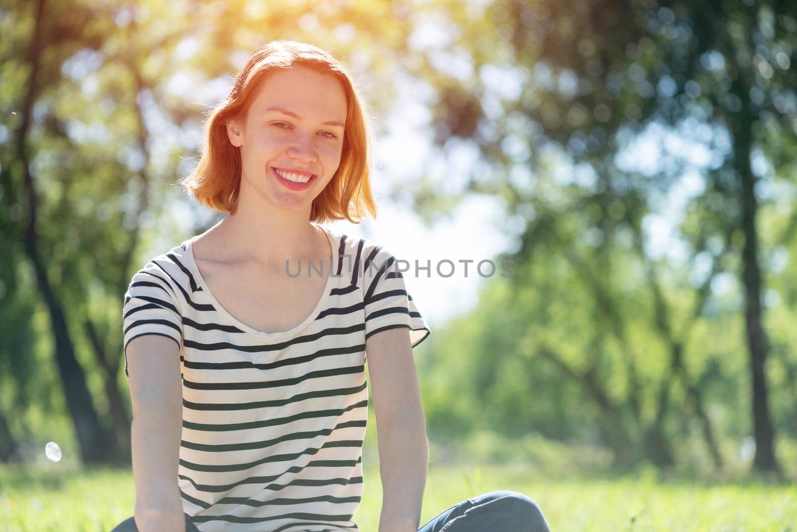 Portrait of a young attractive woman. Sitting cross-legged in the park