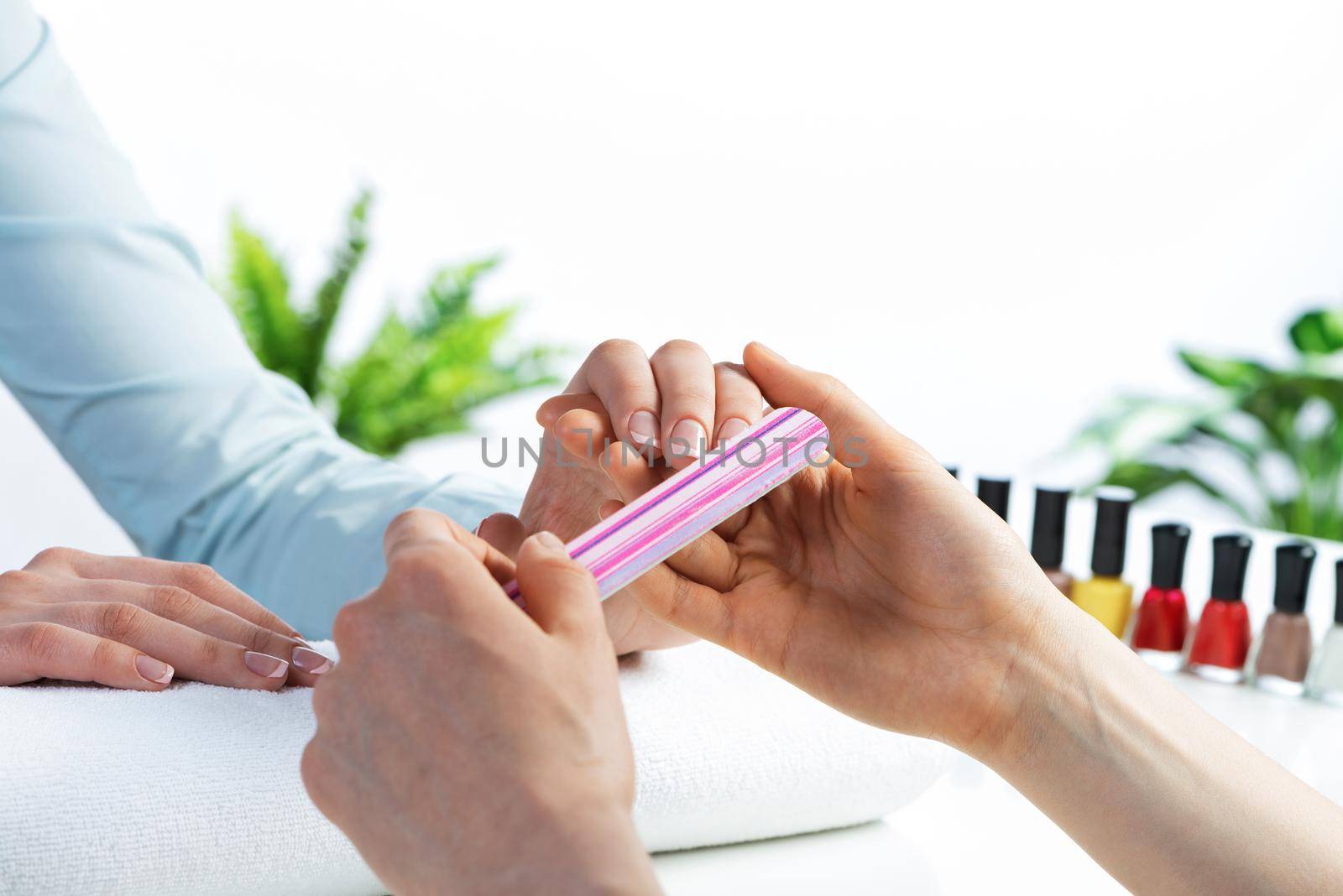 Manicurist using nail file and create perfect nails shape. Closeup of female hand preparing for apply nail polish. Beautician grinding nails with nail file tool. Professional nail art in spa saloon.