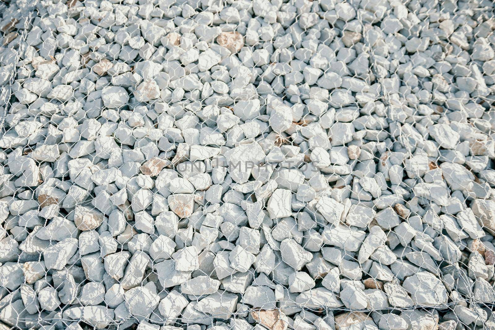strengthening the slope with stones behind the wire. grey texture. construction. Granite stones behind a metal grate
