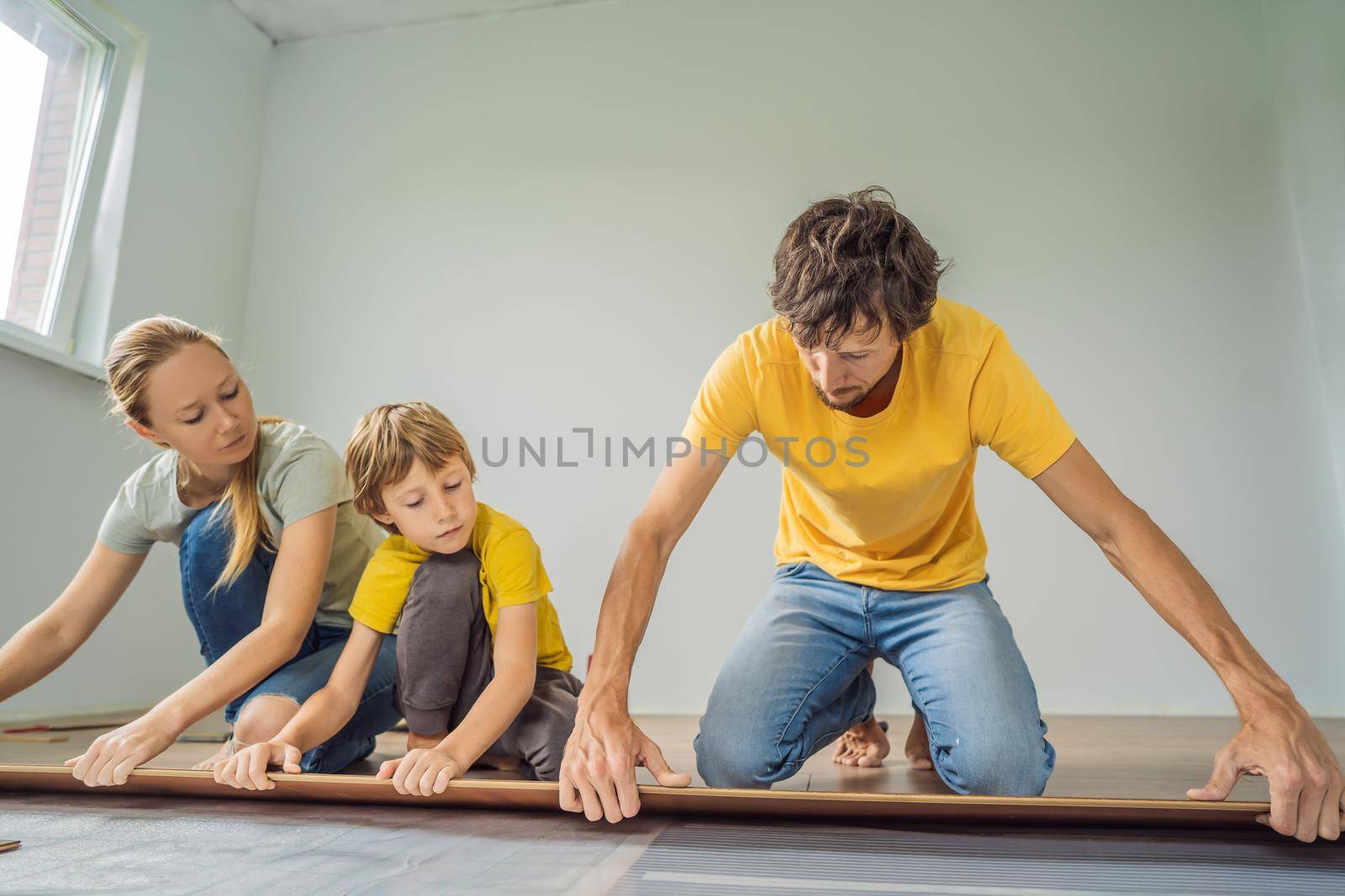 Happy family installing new wooden laminate flooring on a warm film floor. Infrared floor heating system under laminate floor.