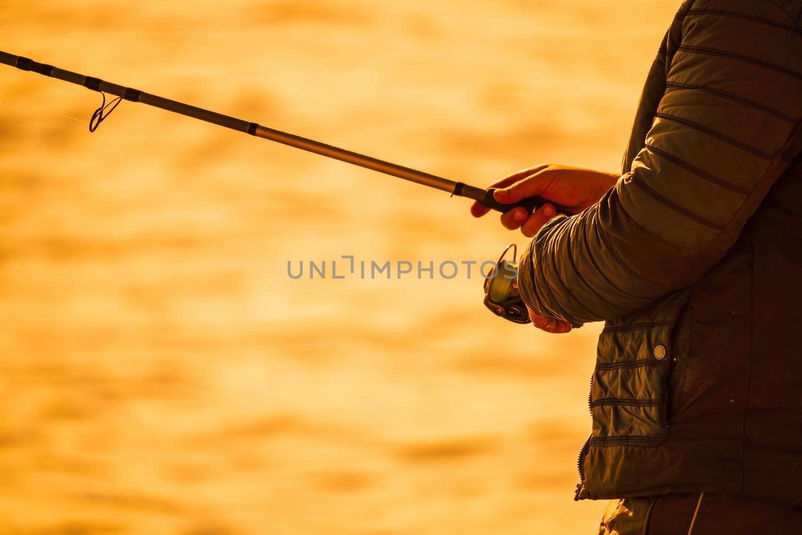 Man hobby fishing on sea tightens a fishing line reel of fish. Calm surface sea. Close-up of a fisherman hands twist reel with fishing line on a rod. Fishing in the blue sea outdoors. by panophotograph