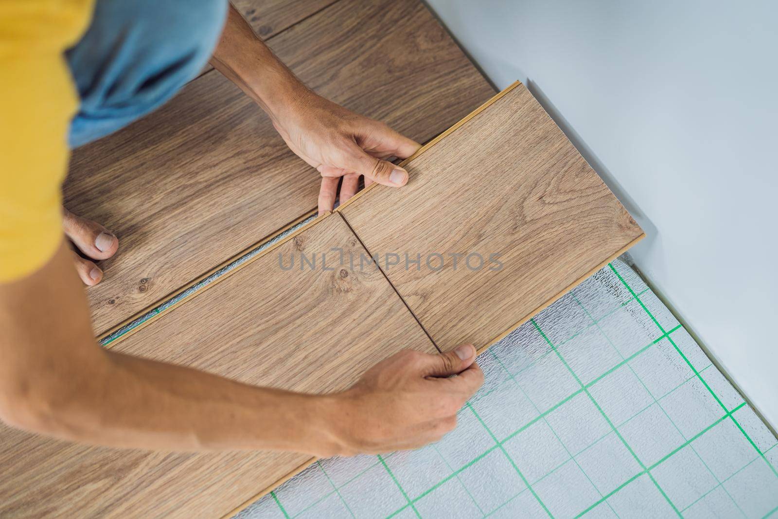 Man installing new wooden laminate flooring on a warm film floor. Infrared floor heating system under laminate floor.