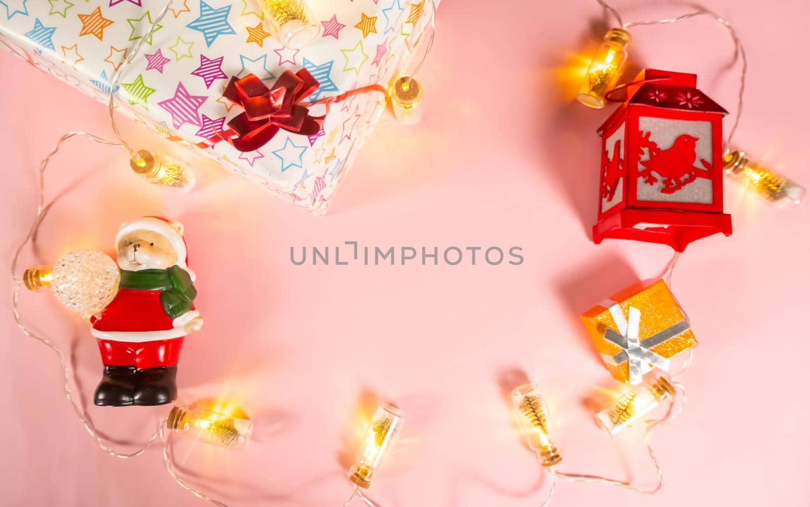 Christmas background - Christmas decorations - a garland, a gift box, a flashlight and a bear in a Santa Claus costume on a light pink background, copy the space. High quality photo