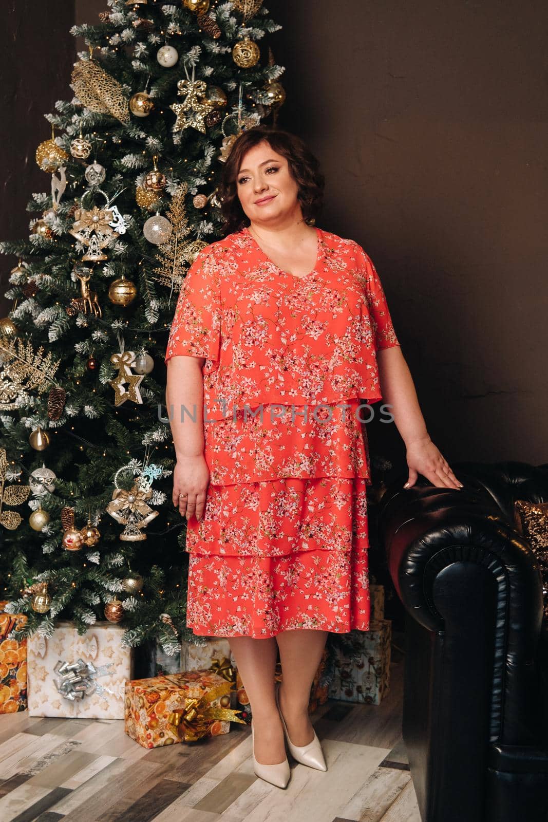 a woman in a red dress standing next to a Christmas tree in an interior decorated for celebrating Christmas and New Year by Lobachad