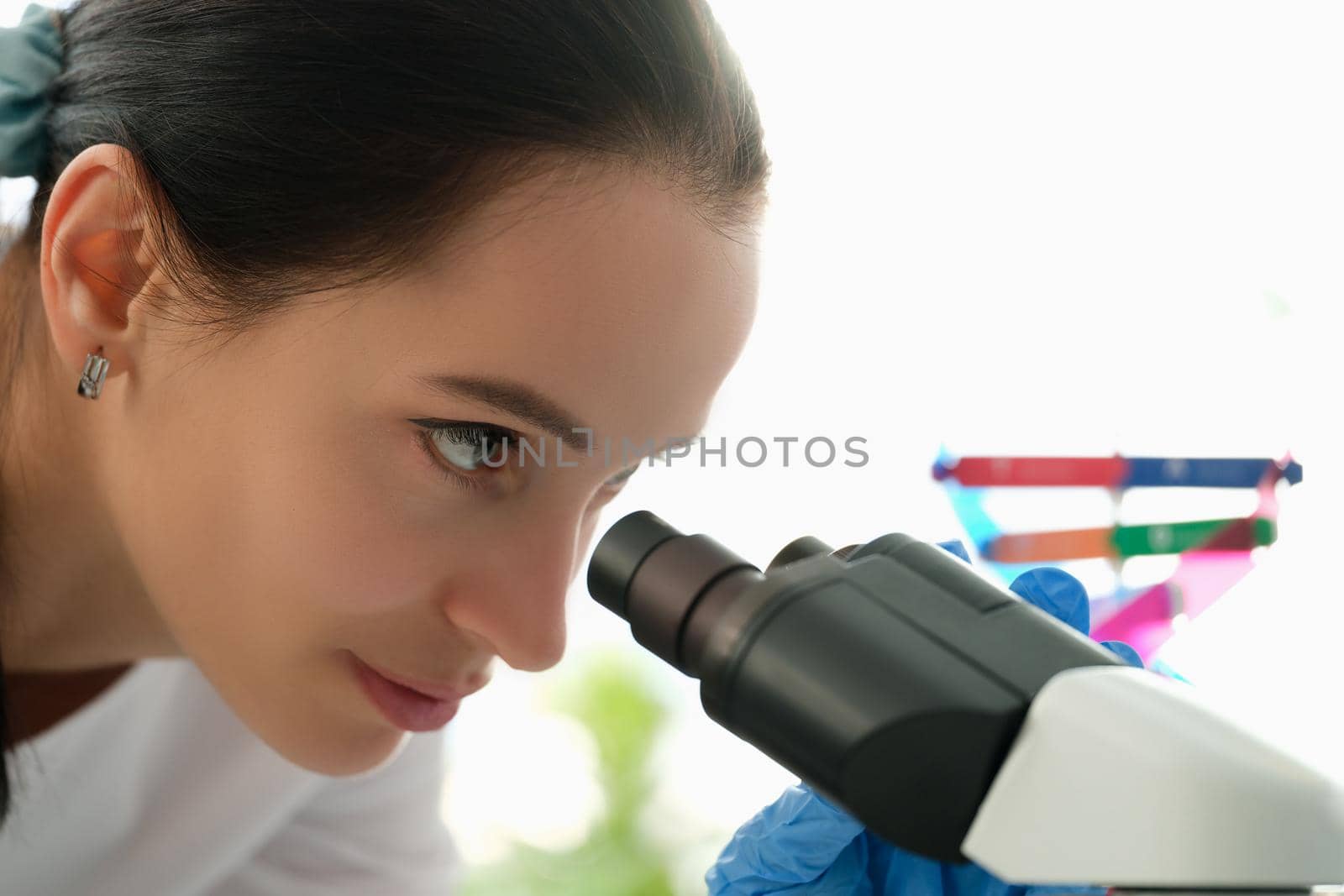 Beautiful woman looks through a microscope, profile view, close-up. DNA research, genetics. Chemical analysis of cells