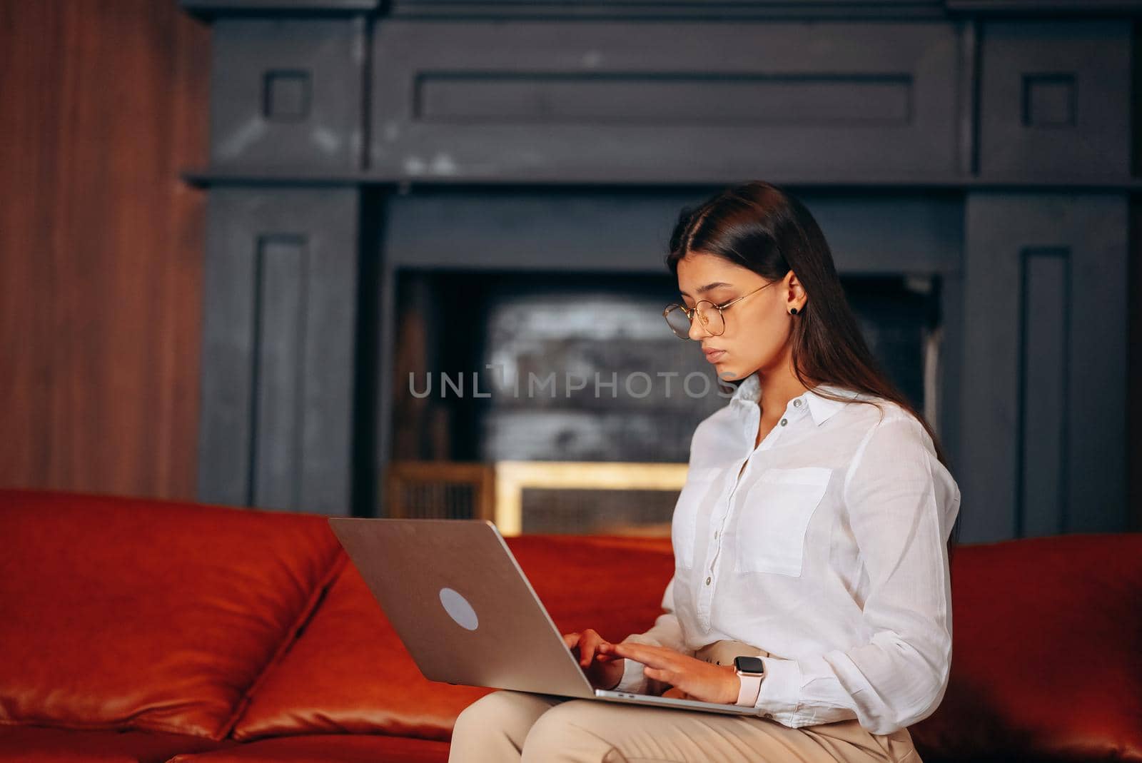 Young woman sits on a red sofa while working at a laptop. Woman hands typing on laptop keyboard.