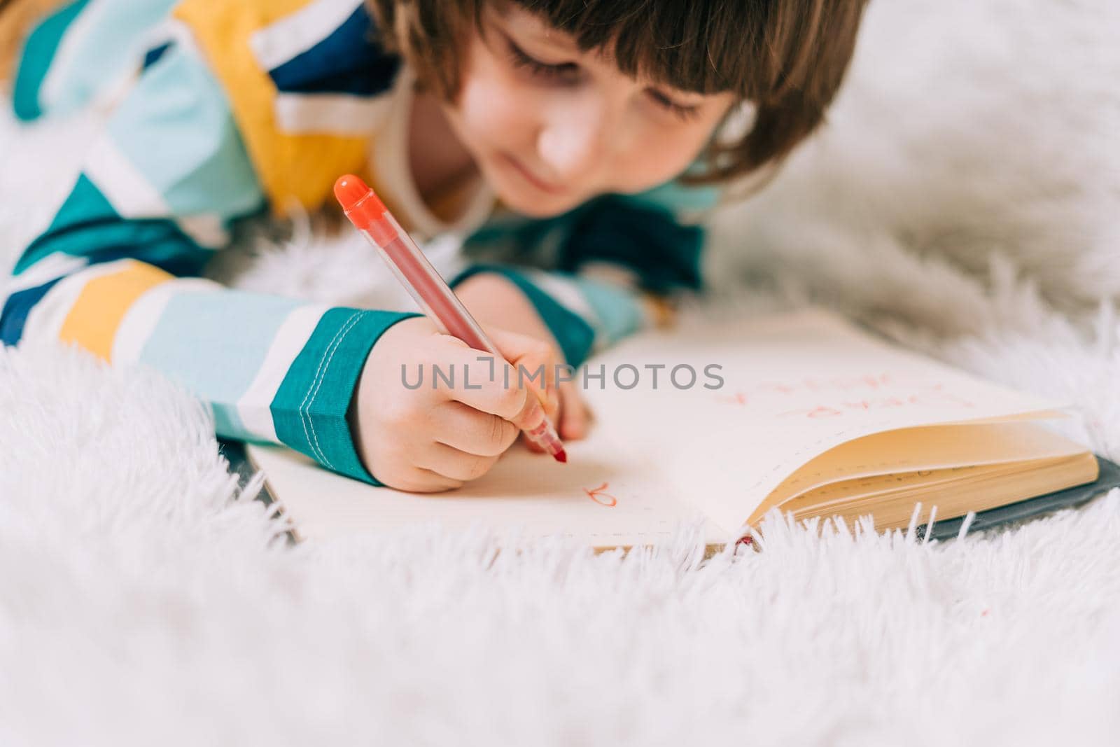Close up hands of Kid boy, lying on couch and writing letter in note pad to dear Santa at home in Christmas holidays. Child wish list. Dreams of a Christmas gifts. Merry Christmas and Happy new year