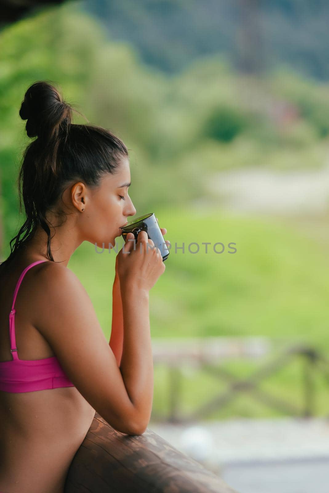 Side view portrait of a happy woman in pink swimsuit contemplating from balcony with coffee cup