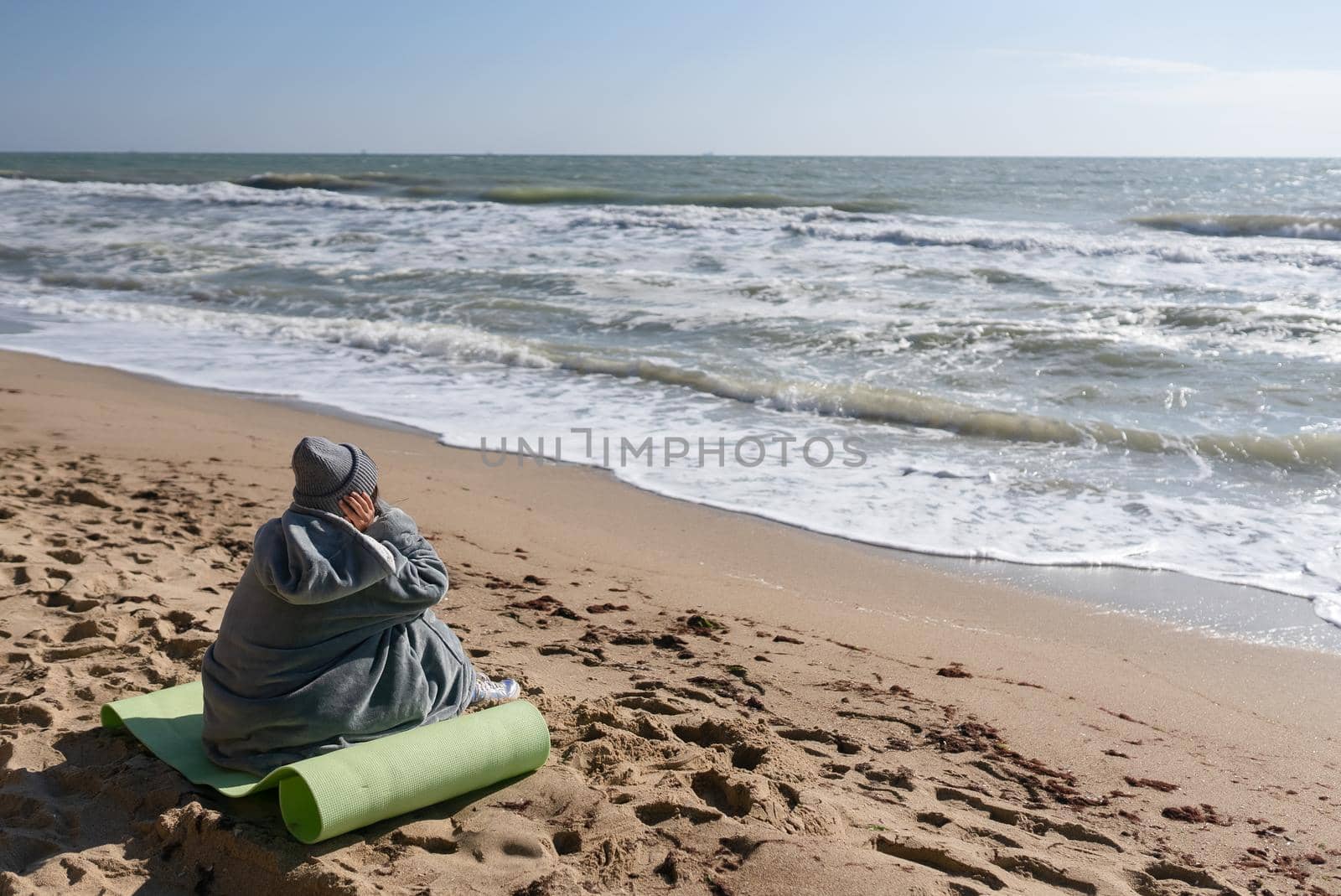 Pretty woman in warm clothes sitting on the cold autumn beach. Copy space.