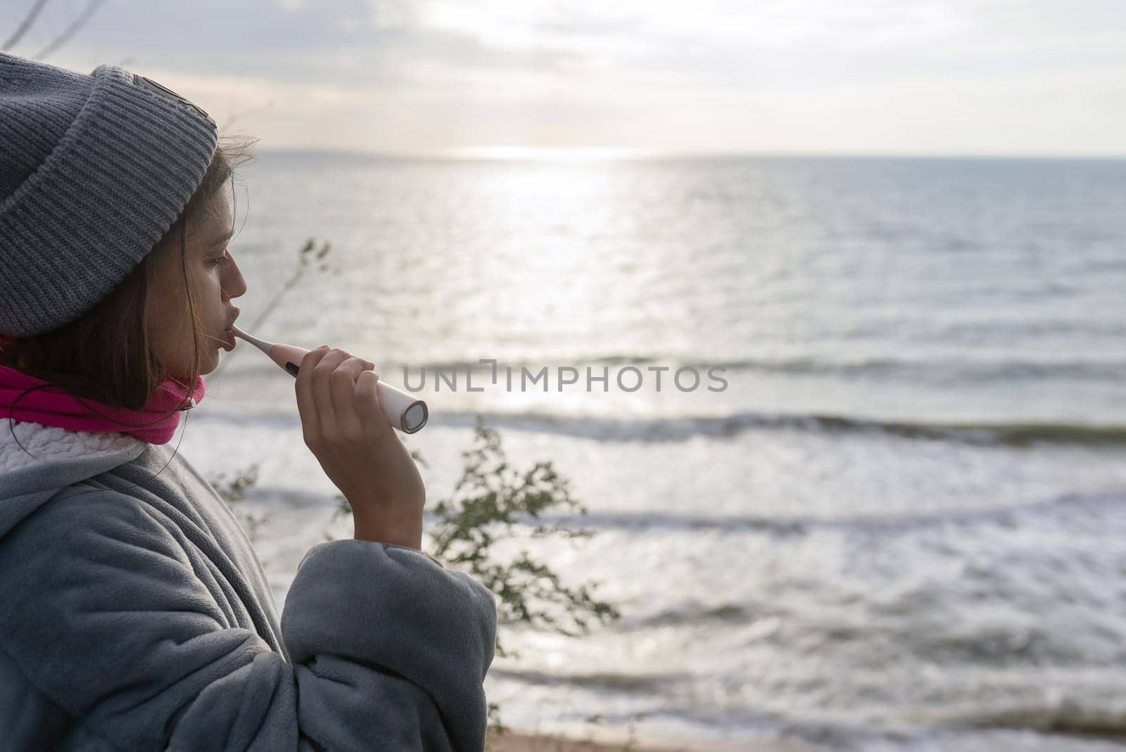 Young woman brushes her teeth with an electric brush on the background of the sea