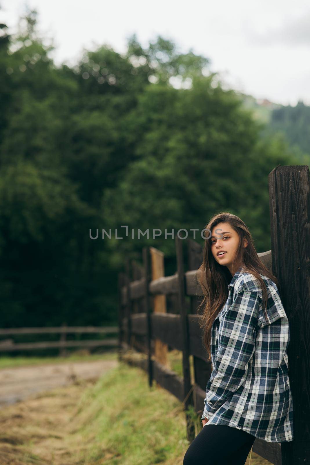 A young attractive Caucasian female stand by a fence and posing at camera