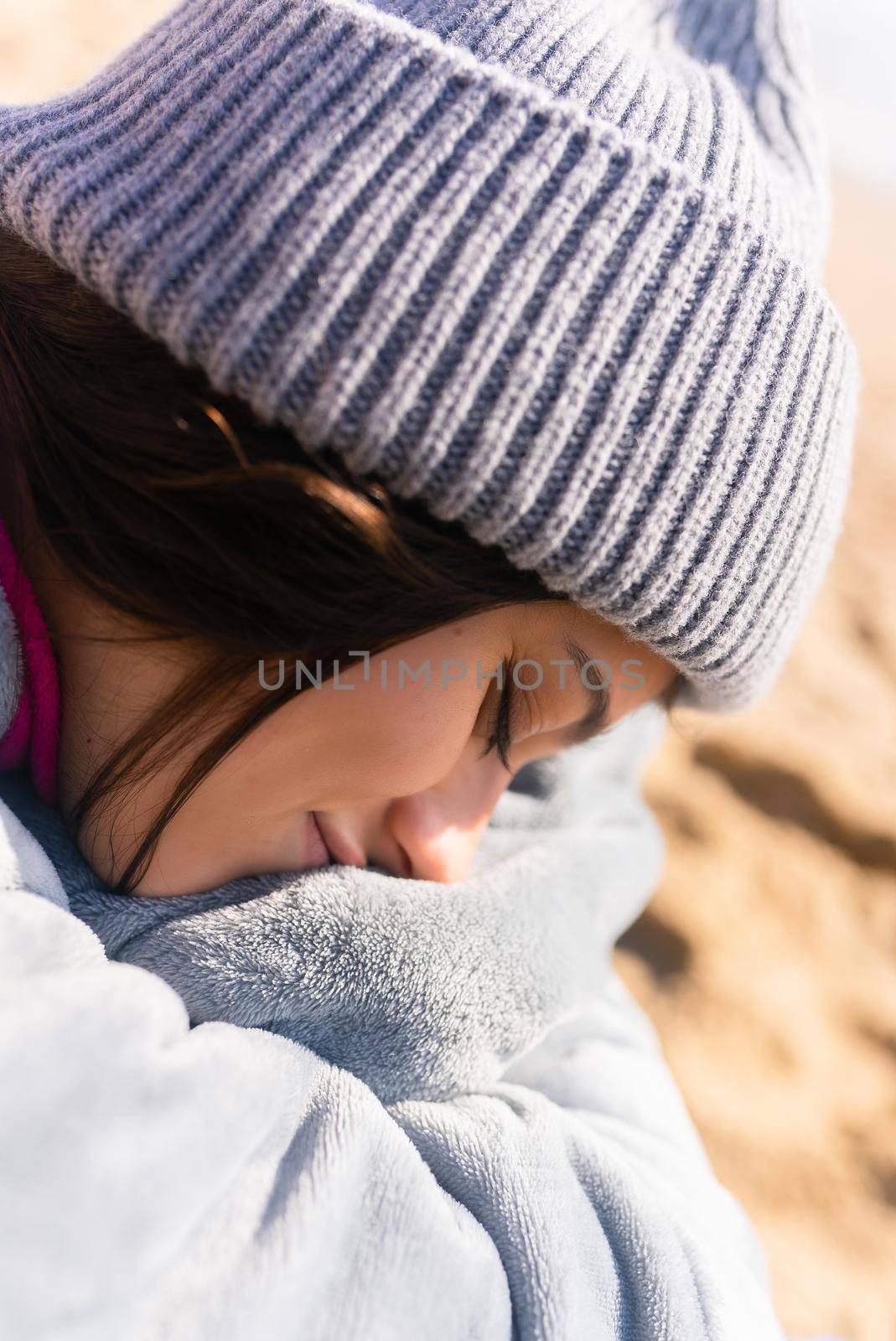 Pretty woman in warm clothes sitting on the cold autumn beach.