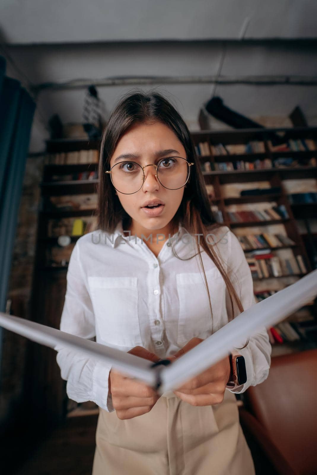 Young woman holding an open book in hands and looking at the camera