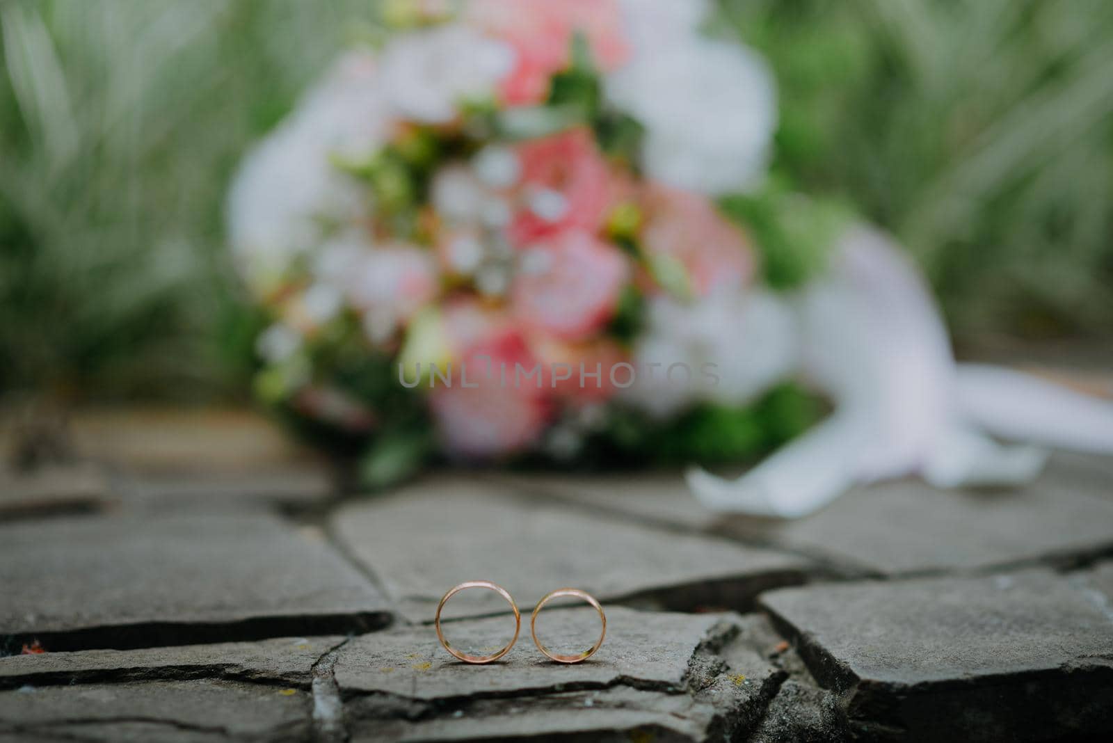 WEDDING GOLD RINGS AND BRIDAL BOUQUET OF FLOWERS ON STONE BACKGROUND. White and pink wedding bouquet of roses and pair of wedding rings on it