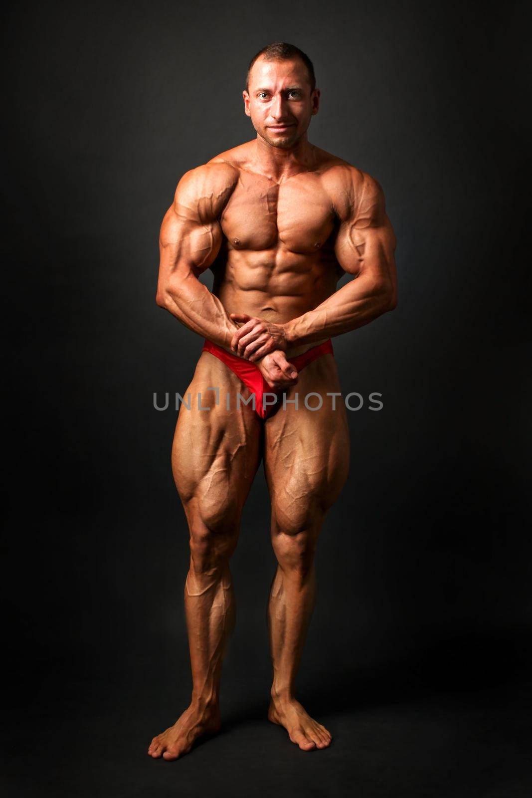 Studio shot of young male bodybuilder on black background, posing, flexing his chest, abs and legs muscles, showing huge biceps.