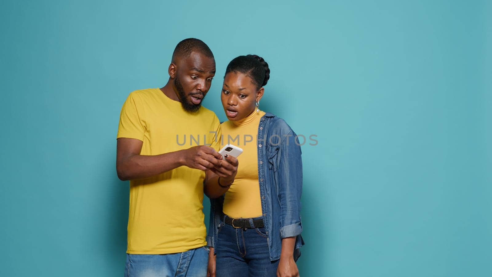 Man and woman using internet on smartphone together in front of camera. People looking at mobile phone display and having positive connection. Modern couple working with technology.