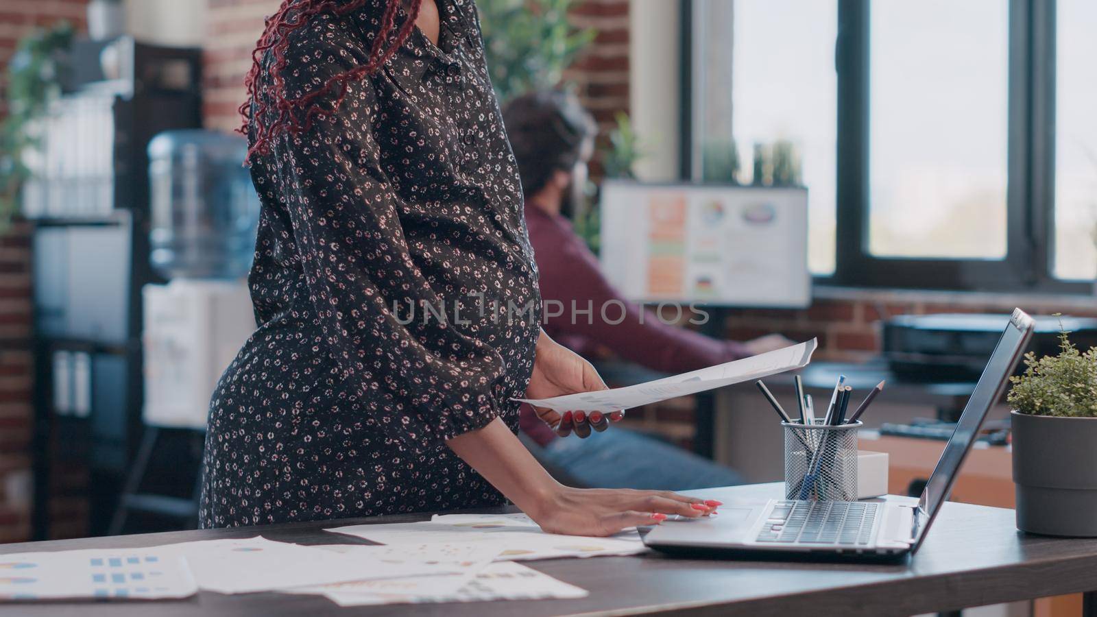 Close up of pregnant business woman holding hand on belly while working on project planning and marketing strategy. Employee expecting baby and designing data analysis on files in office.