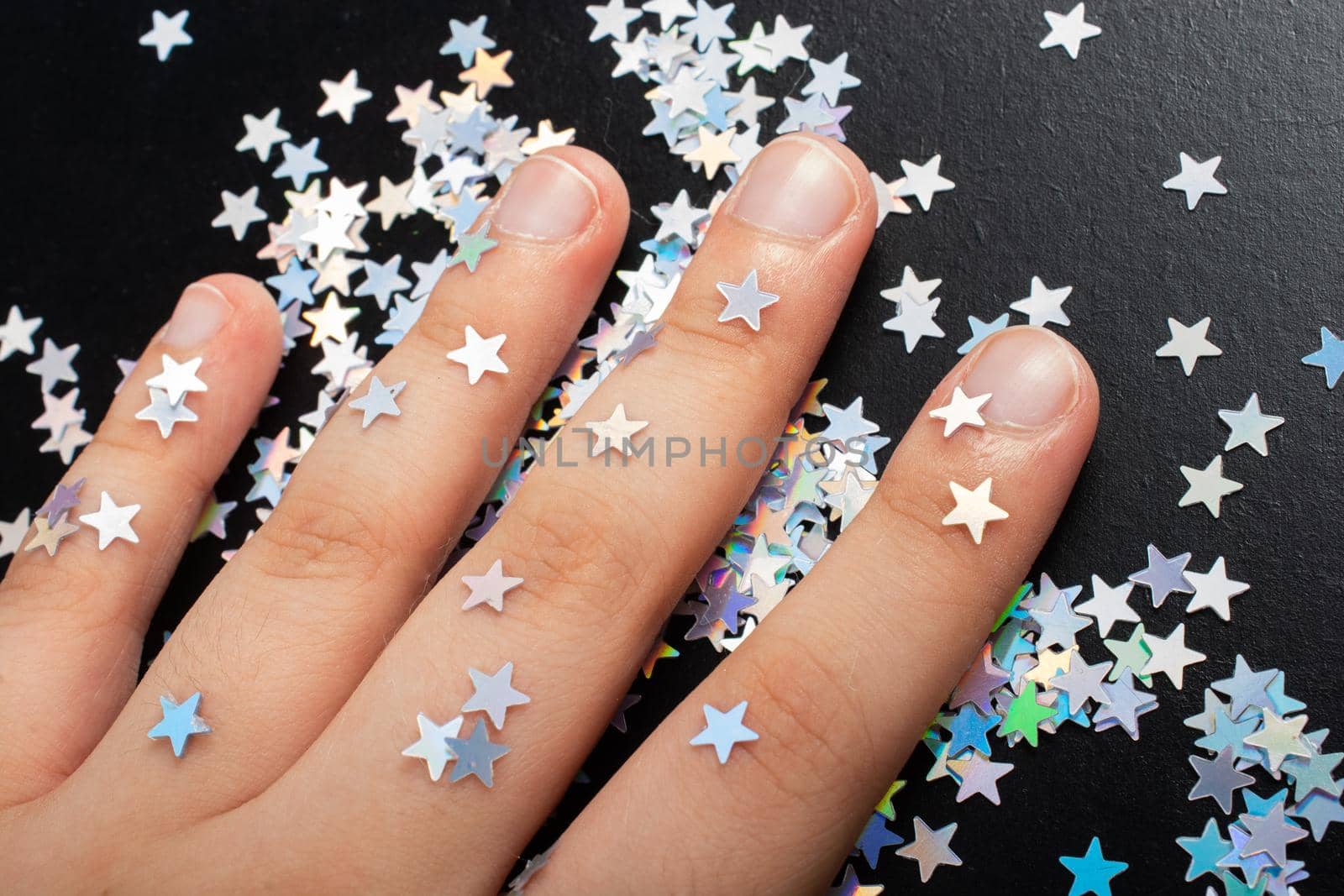 Hand on colorful confetti stars on a dark color background by berkay