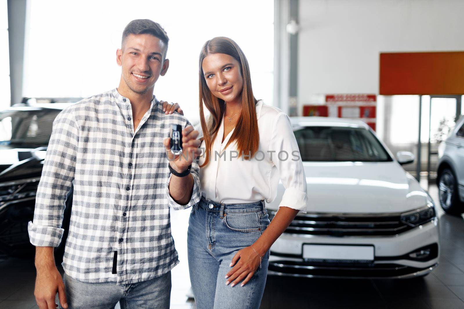 Young happy couple just bought a new car in a dealership showroom