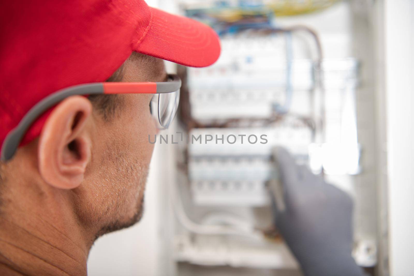 Caucasian Electrician Wearing Safety Glasses Looking Inside Electric Breaker Board For Potential Issues. Residential Electric Circuit.