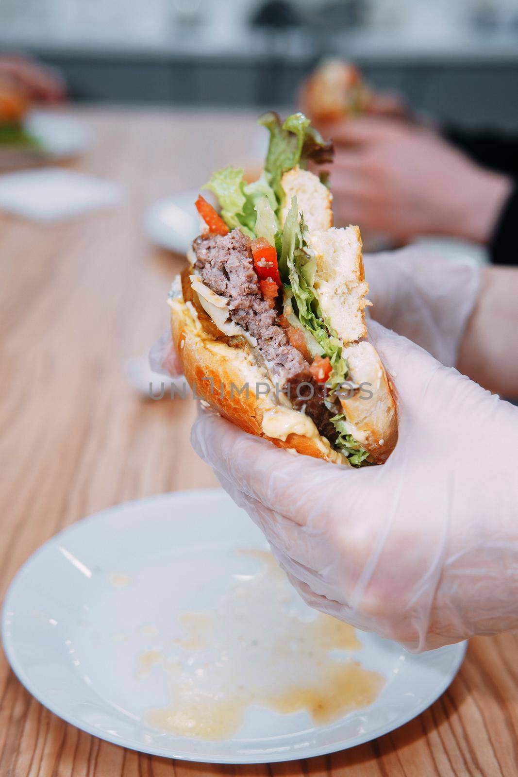 Gloved hands hold a burger while eating. Burgers with beef and vegetables. Delicious hamburgers at the culinary master class. Burger with onion sauce.